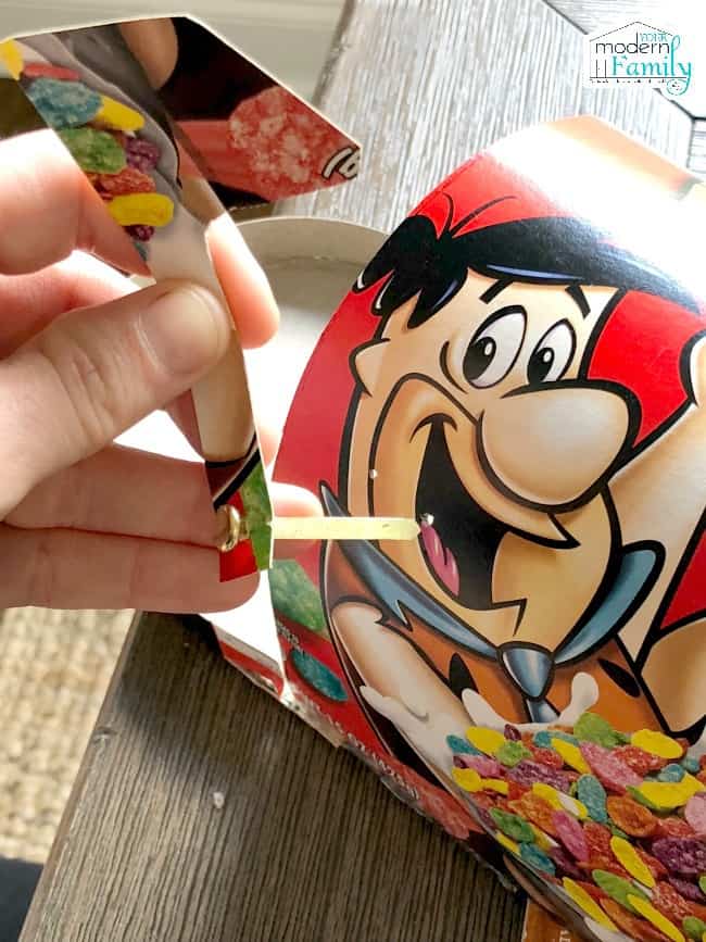 A person\'s hand adding a flag to the mail box made with a cereal box.