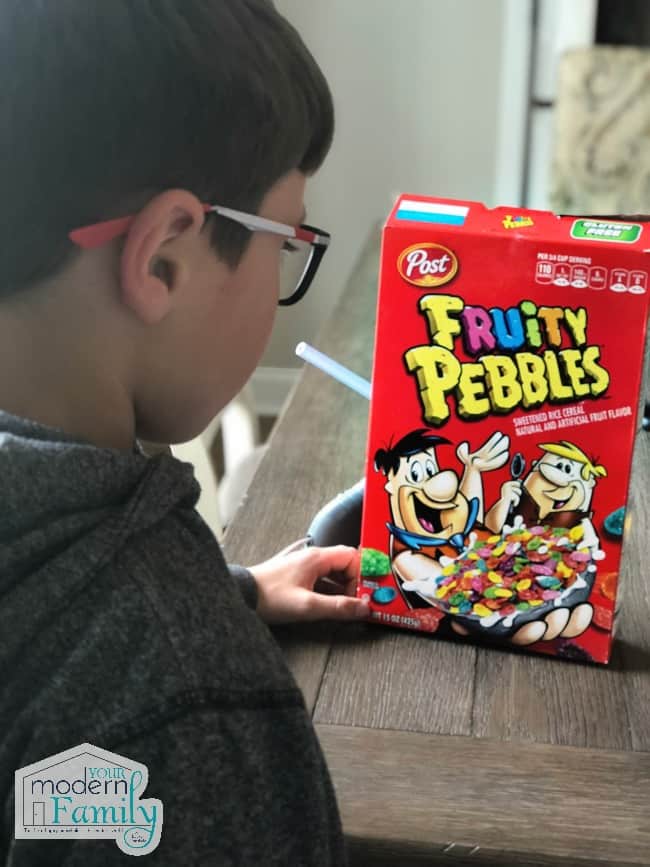 A boy looking at a box of Fruity Pebbles at the table.