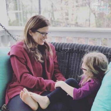 A woman talking to a little girl while sitting on a wicker porch swing.
