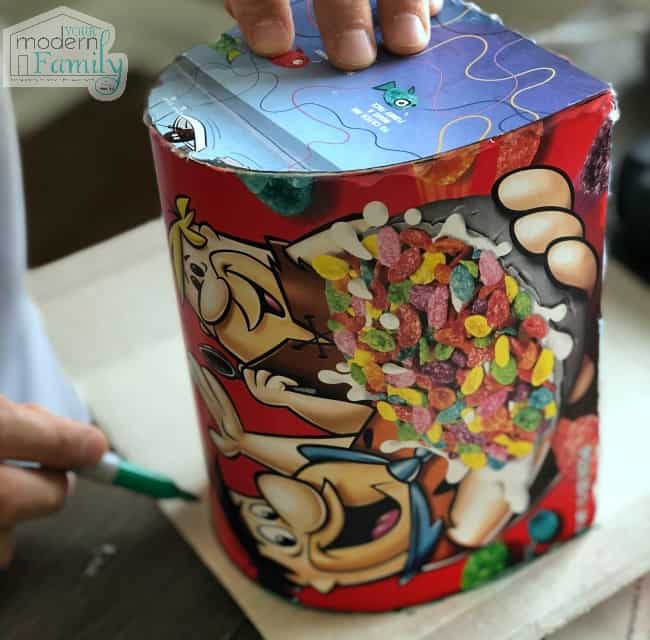 A close up of someone building a paper mail box made from a cereal box.
