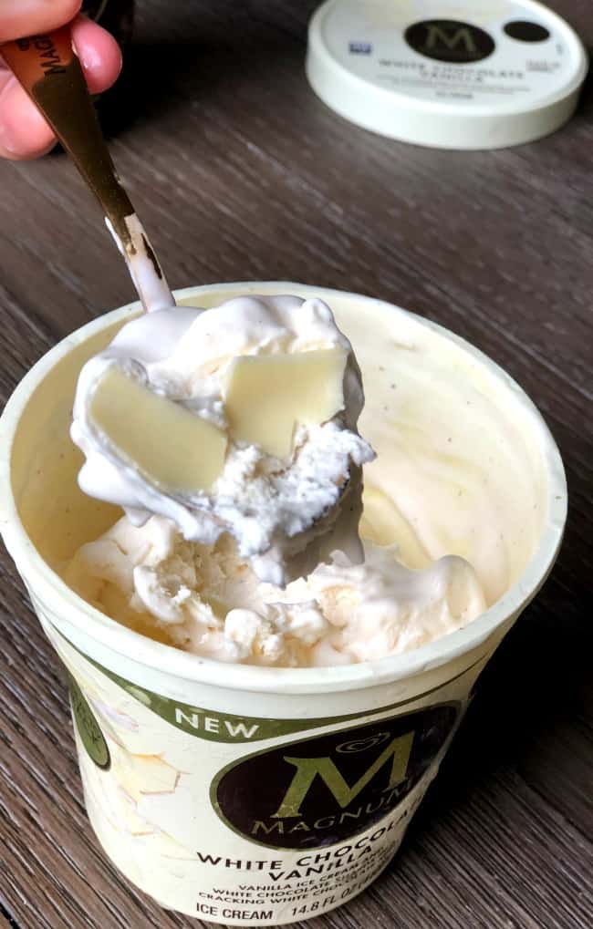  A container of ice cream with a spoon resting on the rim.