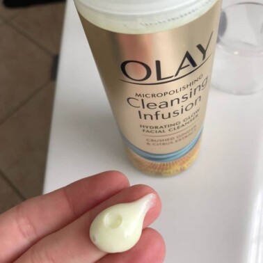 A close up of a bottle of Olay Cleansing Infusion with a dollop of the product on a woman's finger tip.
