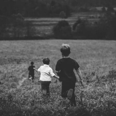 Little boys running down a hill of tall grass.