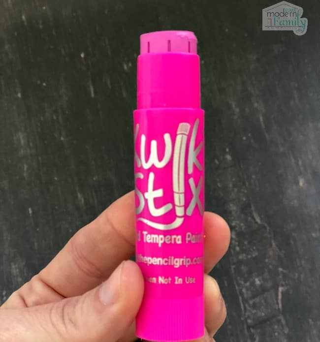 A pink Kwik Stix painting stick being held in a child\'s hand.