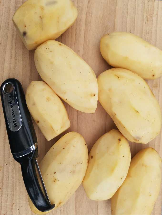 Numerous peeled potatoes and a black peeler sitting on a table.