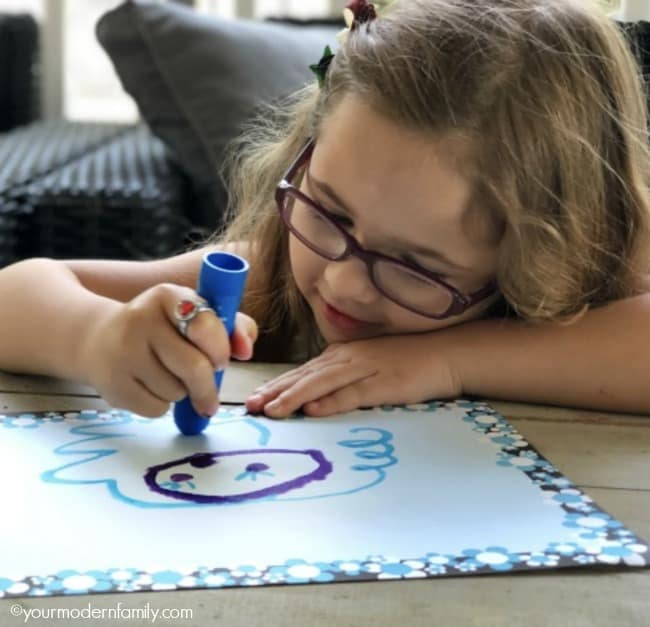 A girl sitting at a table coloring with a blue marker.