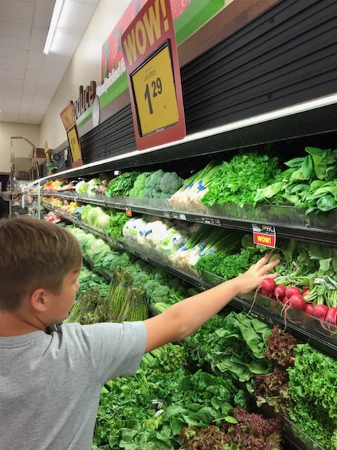 A young boy reaching for produce in a grocery store.