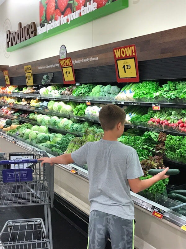 A boy standing in front of a produce stand.