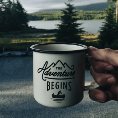 A close up of a cup of coffee with a lake and trees behind it.