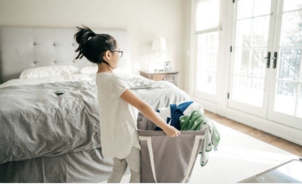 a young girl carrying a laundry bag in a bedroom