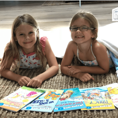Two little girls lying on the floor reading books.