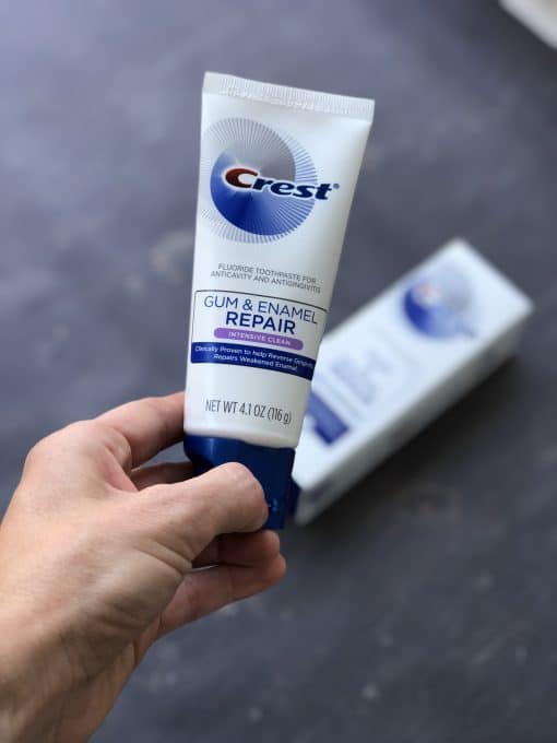 A close up of a person holding a tube of Crest with the box in the background.