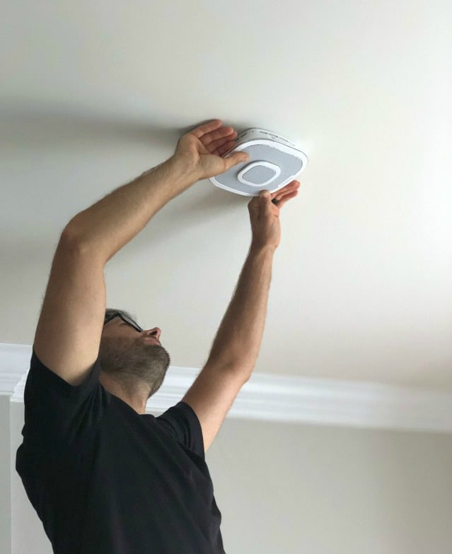 A man installing a  smoke detector on the ceiling.