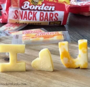 Cheese cut into to shapes and letters standing on a table with the bag of cheese behind them.