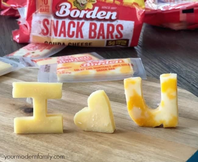 Cheese cut into to shapes and letters standing on a table with the bag of cheese behind them.