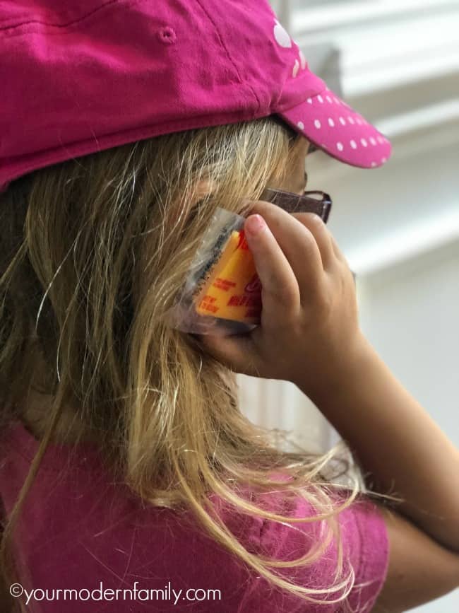 A little girl holding a cheesy snack bar that is in its wrapper decorated like a cell phone to her ear.