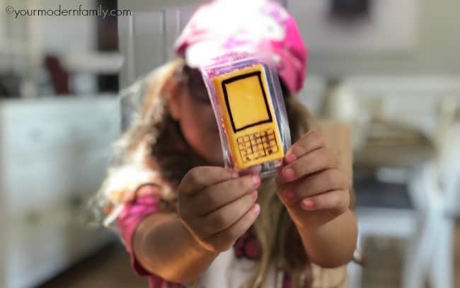 A little girl holding a cheesy snack bar decorated to look like a cell phone.