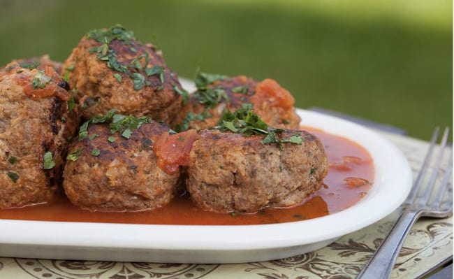A white plate with meatballs and sauce on it.
