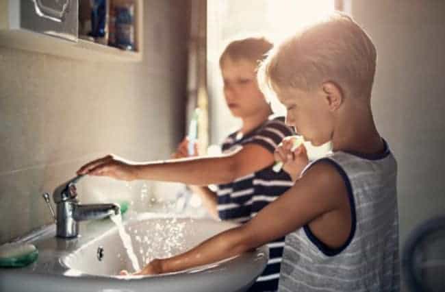 Two children brushing their teeth at the sink.
