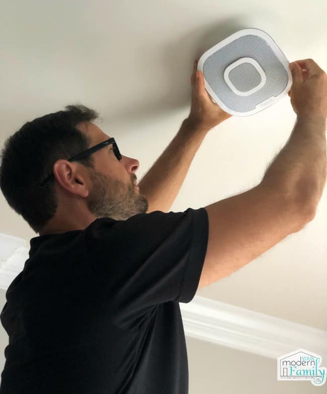 A man installing a smoke detector to the ceiling.