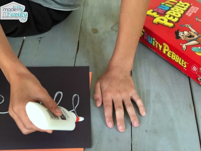 A child squeezing glue onto a black sheet of paper.