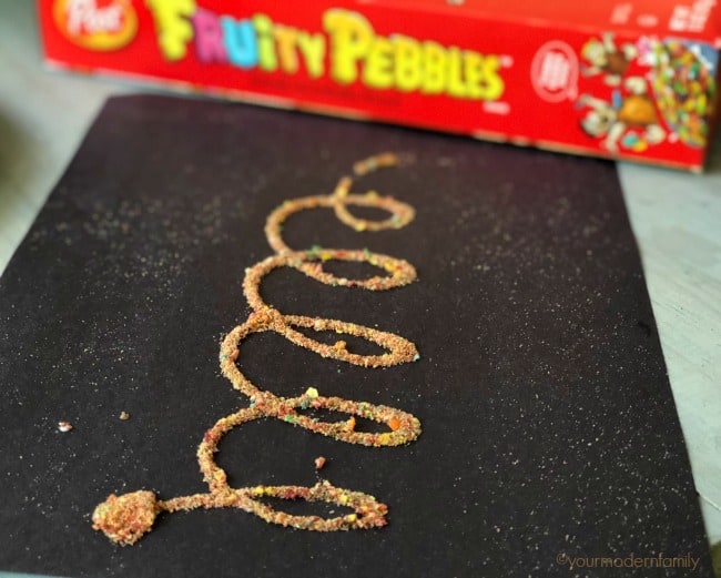 Crushed Fruity Pebbles shaped into a loop rope across a black table.