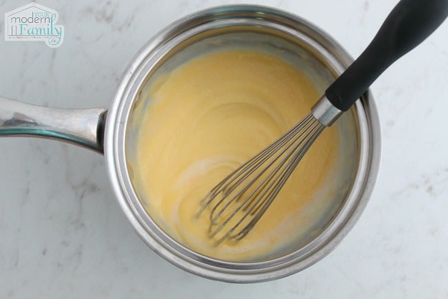 A metal pan with a whisk stirring cheese sauce.
