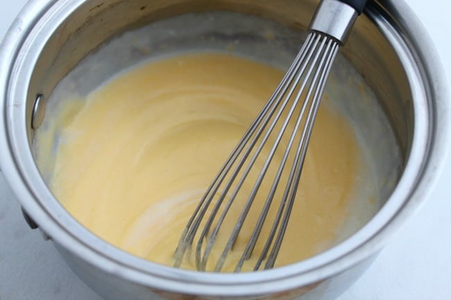 Cheese sauce in a metal pan with a whisk.