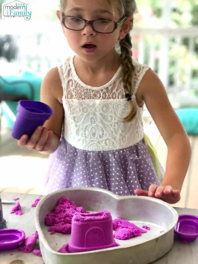 A little girl playing with purple Kinetic sand.
