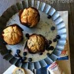 A metal pie pan with three muffins in it with blueberries around them.