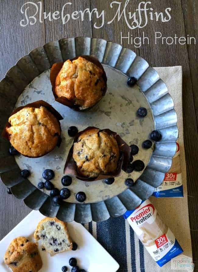 A metal pie pan with three muffins in it with blueberries around them.