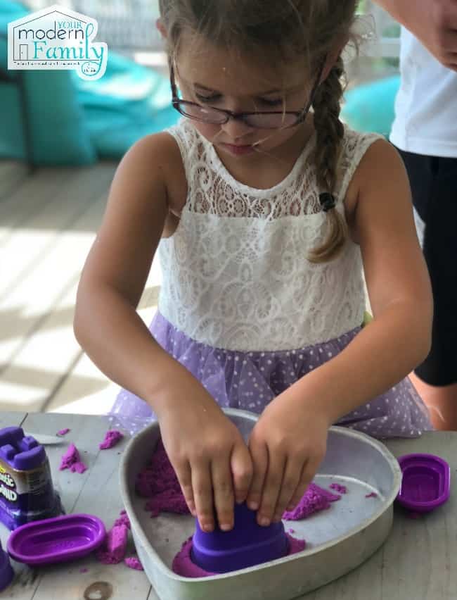 A little girl molding Kinetic Sand in a heart shaped metal pan.