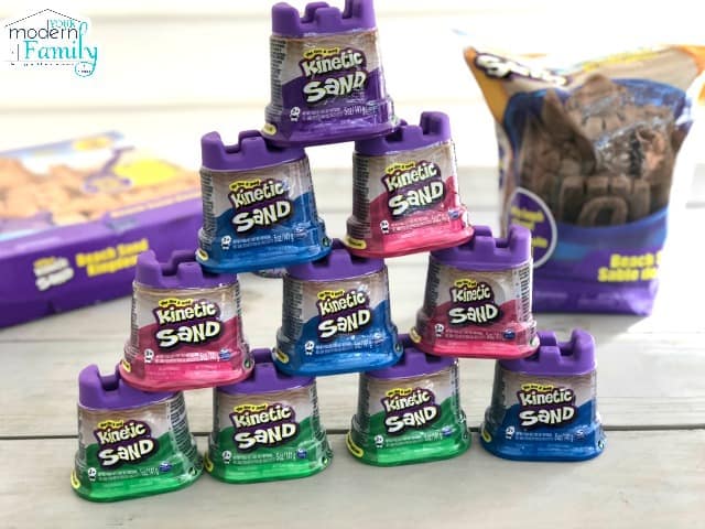 A bunch of containers  of Kinetic Sand that are sitting on a table.