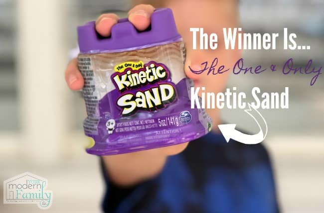 A child holding an unopened container of Kinetic Sand in his hand.