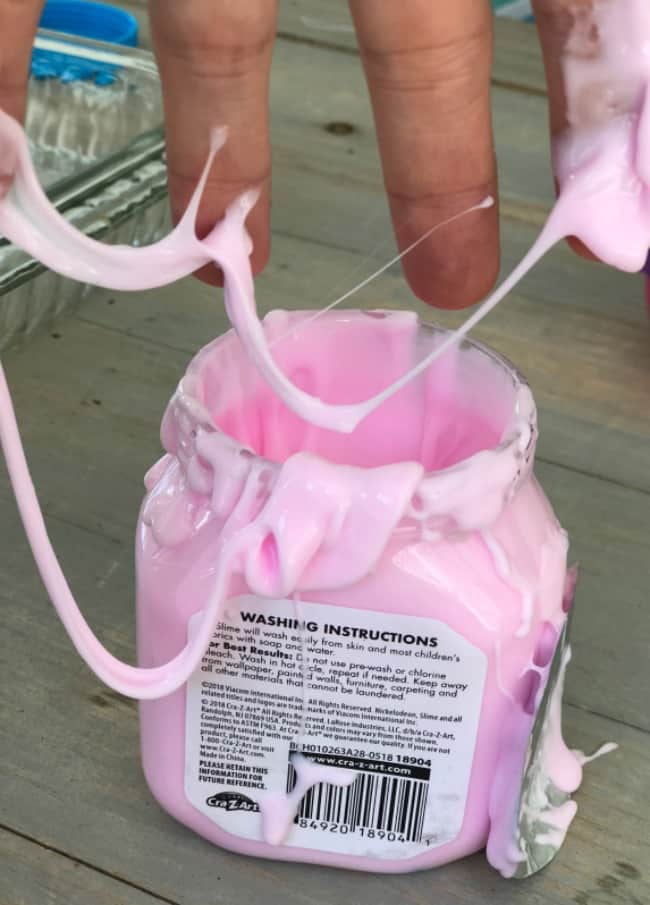 A persons hand with pink kinetic sand dripping off their fingers into a plastic jar.