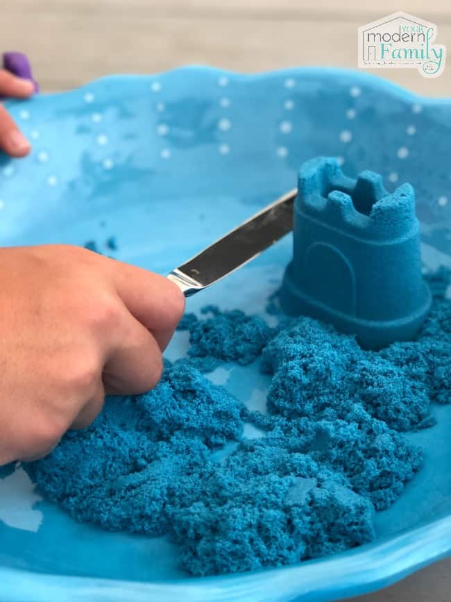 A child cutting blue Kinetic Sand with a knife.
