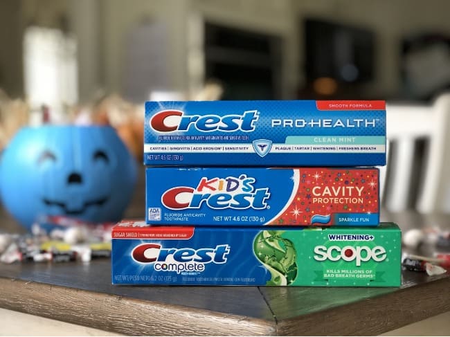 Three boxes of Crest stacked on a table with a blue plastic pumpkin  in the background.
