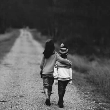 Two people walking down a dirt road with their arms around each other.