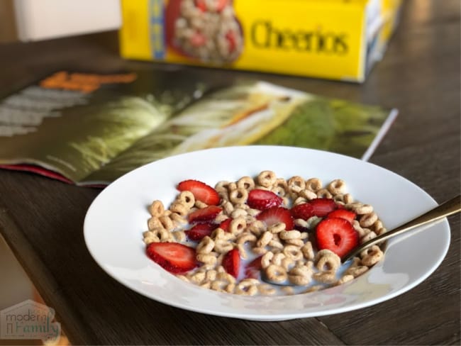 A white bowl with Cheerios, strawberries and milk sitting on a table.