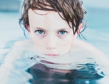 A boy in a pool with his head and shoulders out of the water.