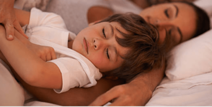 A little boy sleeping in a woman\'s arms.