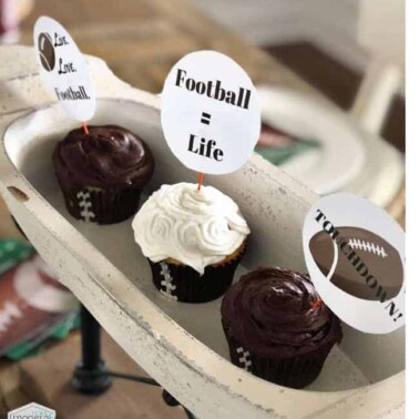 Three cupcakes on a white oval tray with football themed cupcake toppers on them.