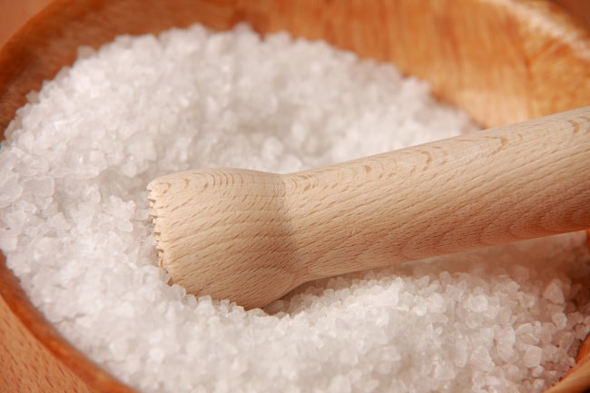 A pile of salt on a wooden table with a wooden utensil resting on the salt.