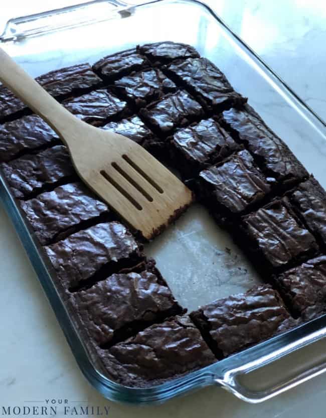 A cookie sheet with brownies that are cut into squares with a spatula resting on them.
