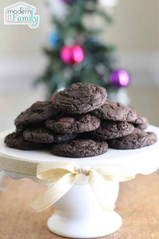 Chocolate cookies sitting on a white plate with a Christmas tree in the background.