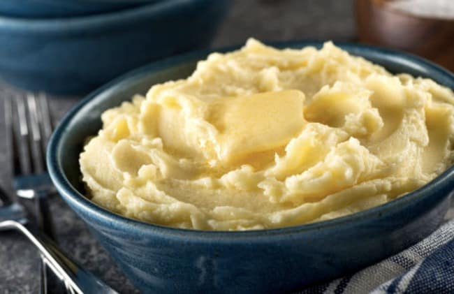Uma tigela de purê de batatas com manteiga por cima.