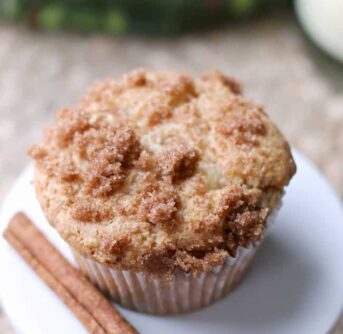 A close up of a muffin sitting on a white plate with a stick of cinnamon sitting beside it.