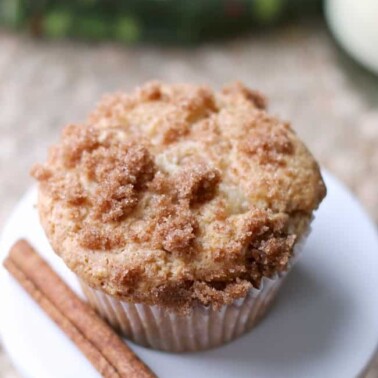 A close up of a muffin sitting on a white plate with a stick of cinnamon sitting beside it.