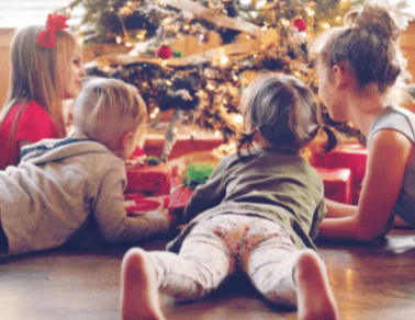 Two children and a woman lying on the floor in front of a Christmas tree.