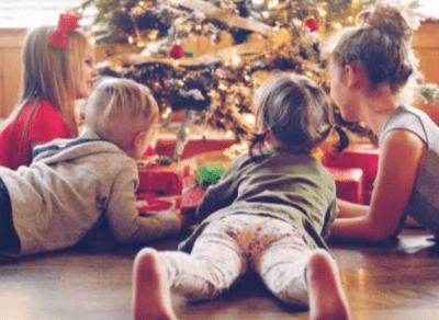 Two children and a woman lying on the floor in front of a Christmas tree.